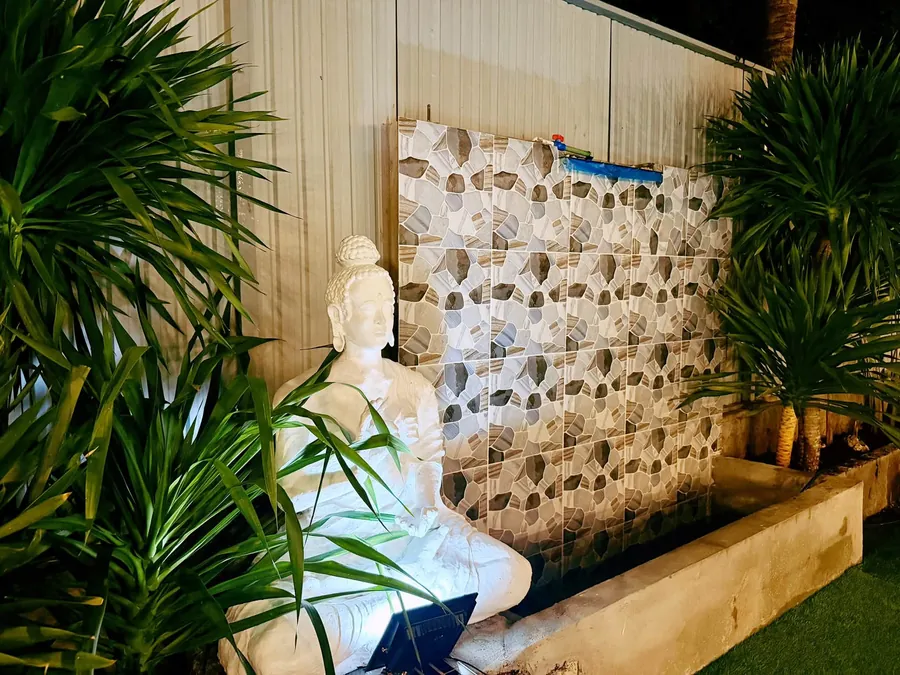 Garden corner with a white Buddha statue and a tiled water wall