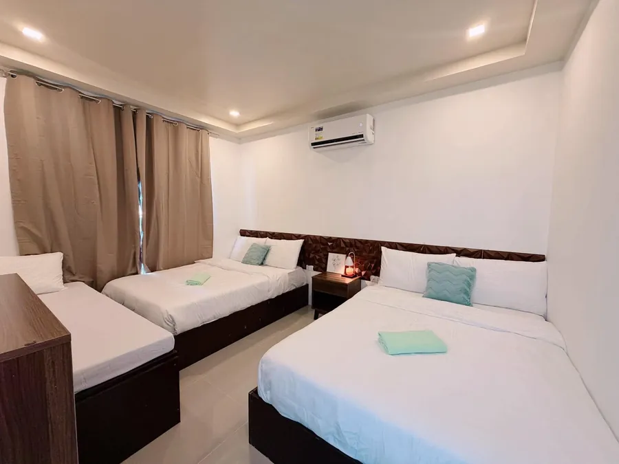 Air-conditioned bedroom with three white-linen beds and beige curtains