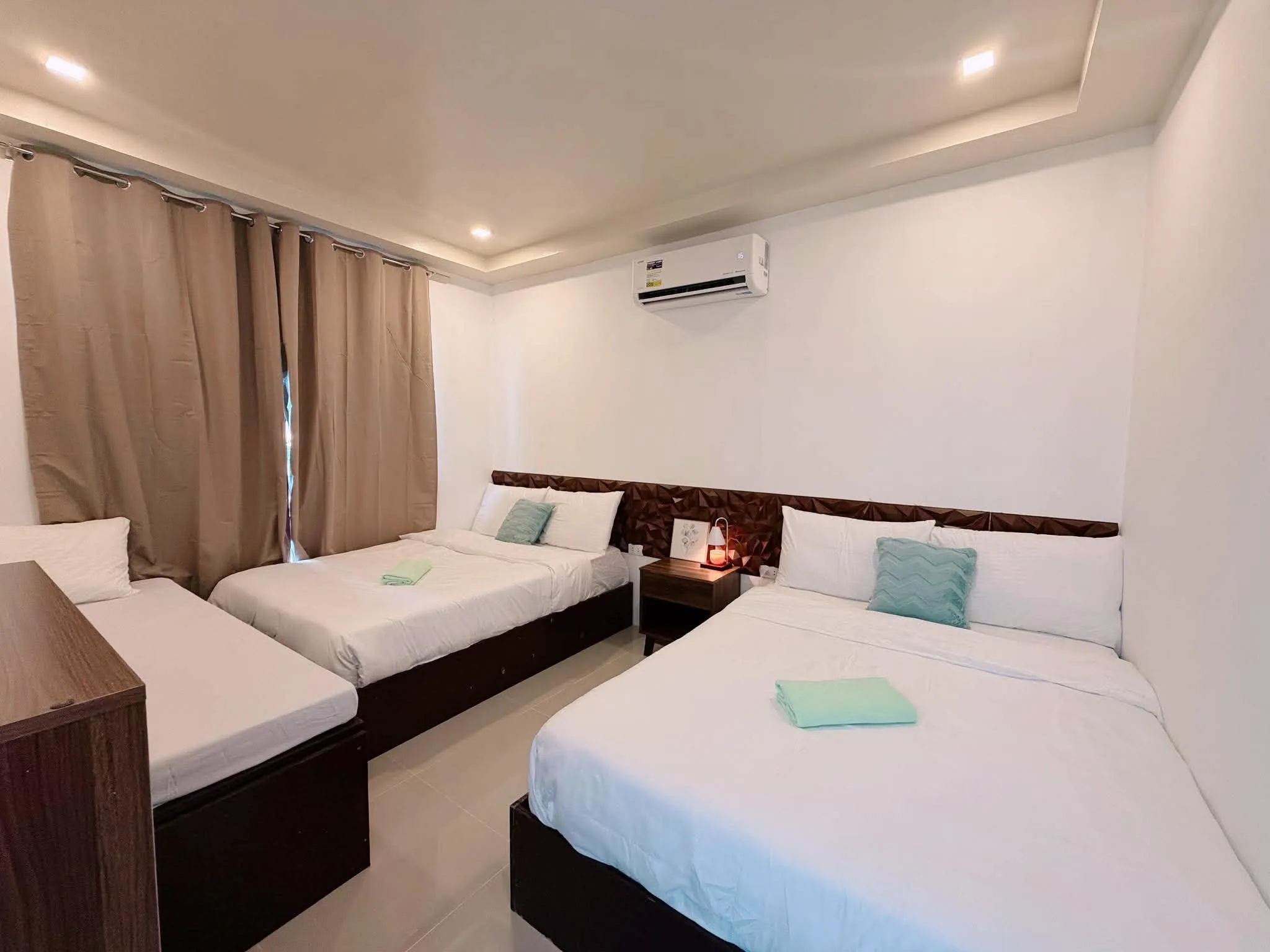 Air-conditioned bedroom with a double bed and two day beds beside a window with beige curtains