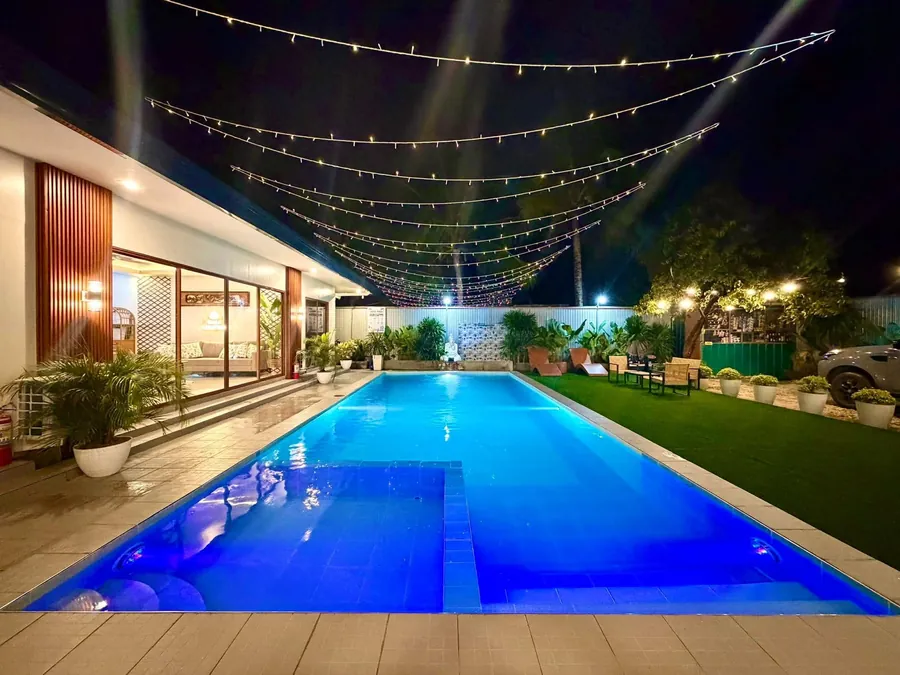 The long pool with string lights, lawn and garden chairs at night