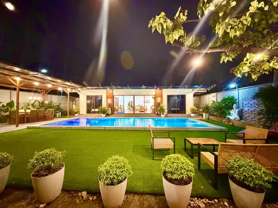 The lawn, garden chairs and pool with the villa behind, lit at night